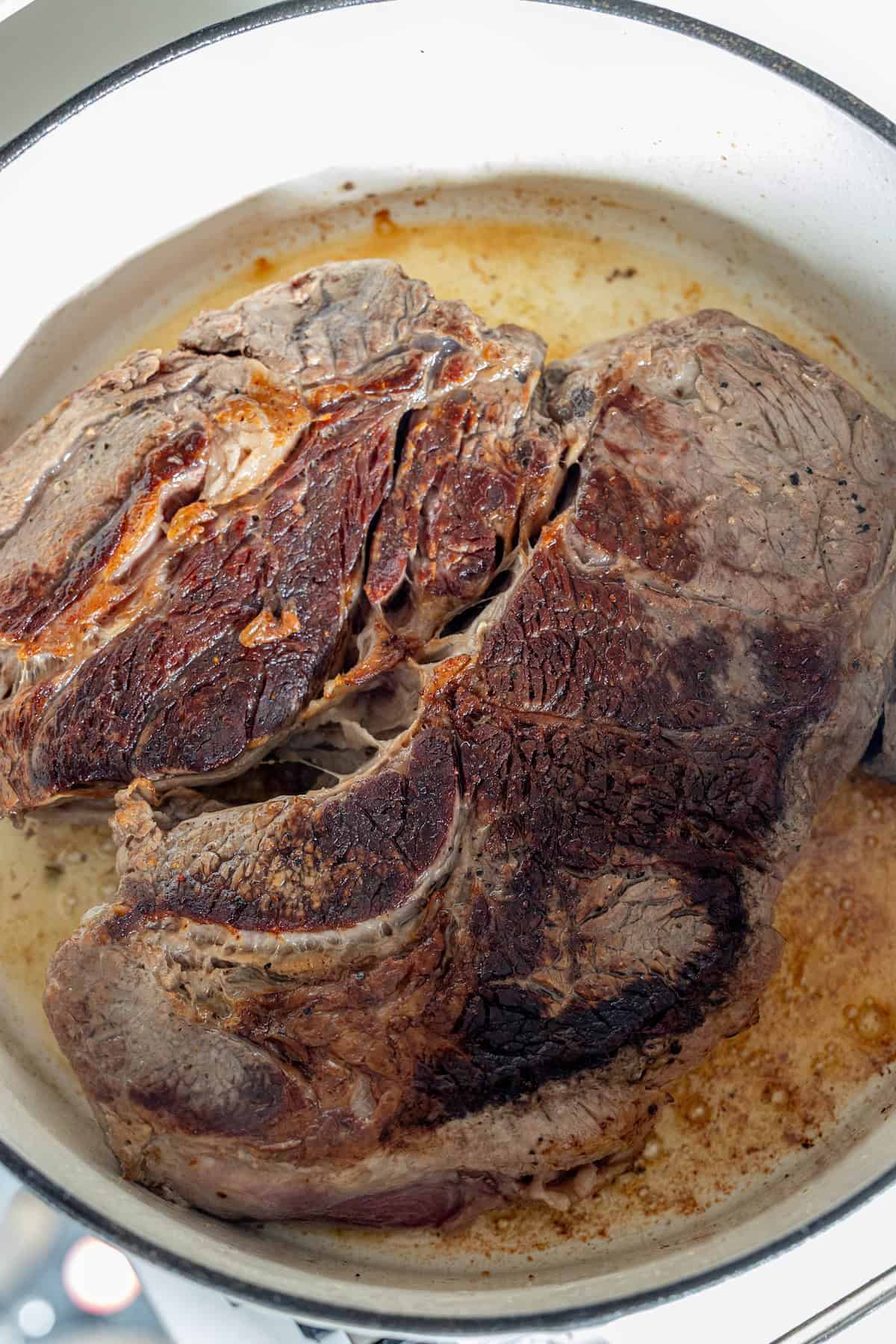 A large piece of seared beef roast browning in a white Dutch oven with visible caramelization and rendered juices, perfect for making an Onion Soup Pot Roast.
