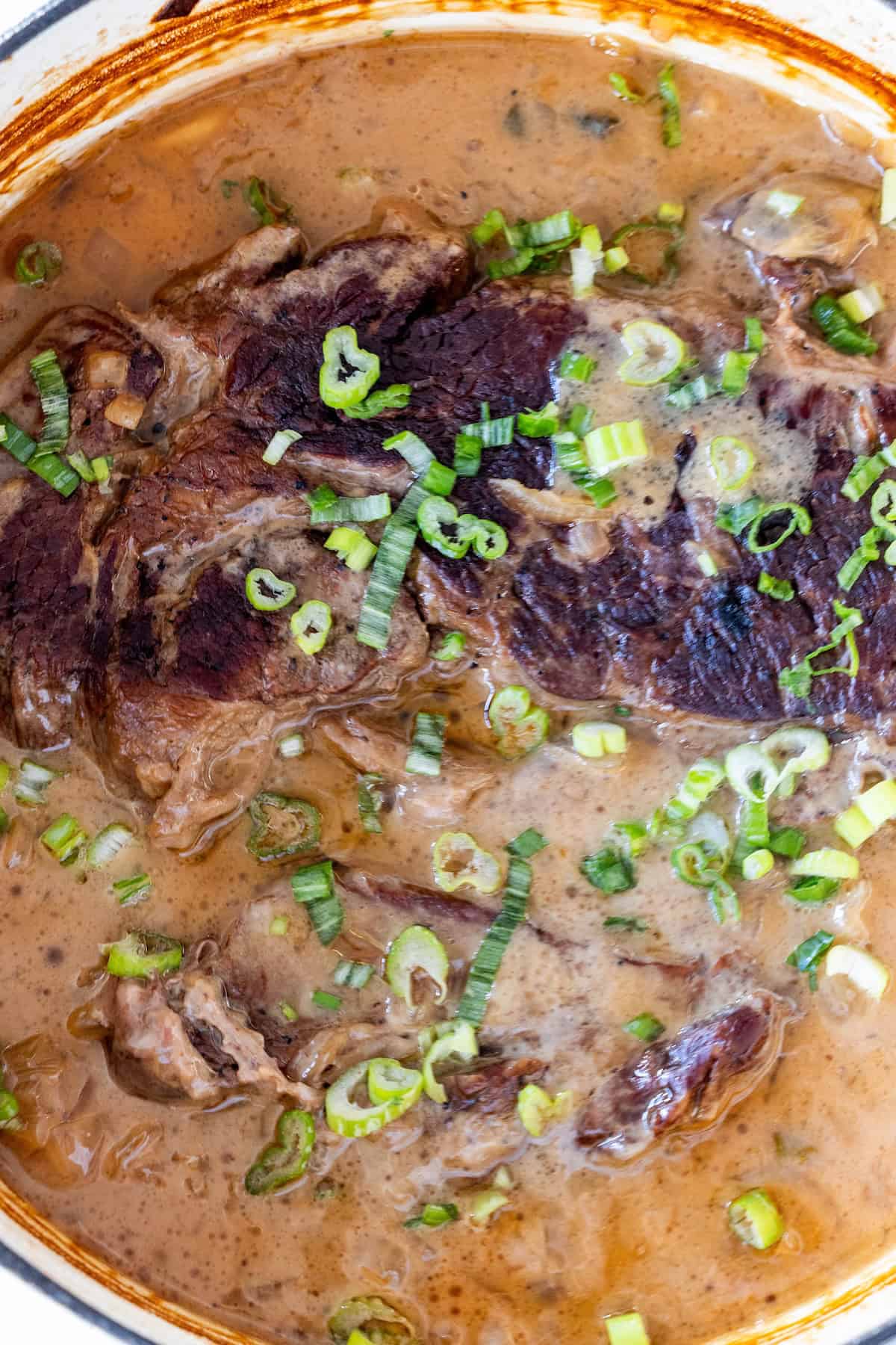 Tender braised beef in a creamy brown sauce is served pot roast style, garnished with chopped green onions—an irresistible take on Onion Soup Pot Roast.