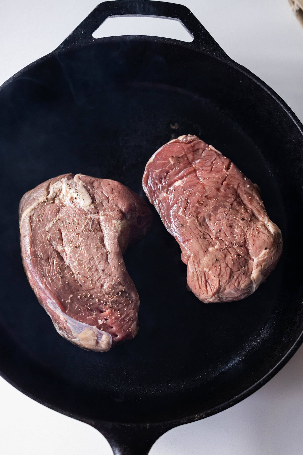 Two raw sirloin steaks are being cooked in a black cast iron skillet, promising the flavor and tenderness of the best sirloin steak.