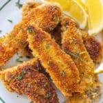 A plate of golden-brown breaded and fried fish fillets garnished with chopped herbs, served with lemon wedges.