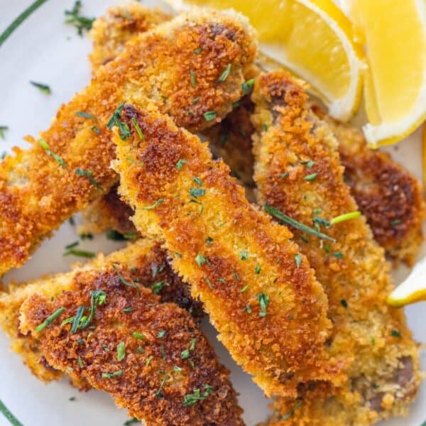 A plate of golden-brown breaded and fried fish fillets garnished with chopped herbs, served with lemon wedges.