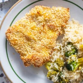 A plate with breaded baked chicken breast and a serving of white rice mixed with broccoli, similar to the style of baked breaded pork chops.