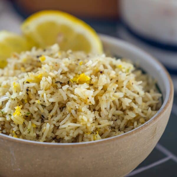 A bowl of Baked Lemon Rice garnished with herbs and lemon zest, with two lemon wedges in the background.