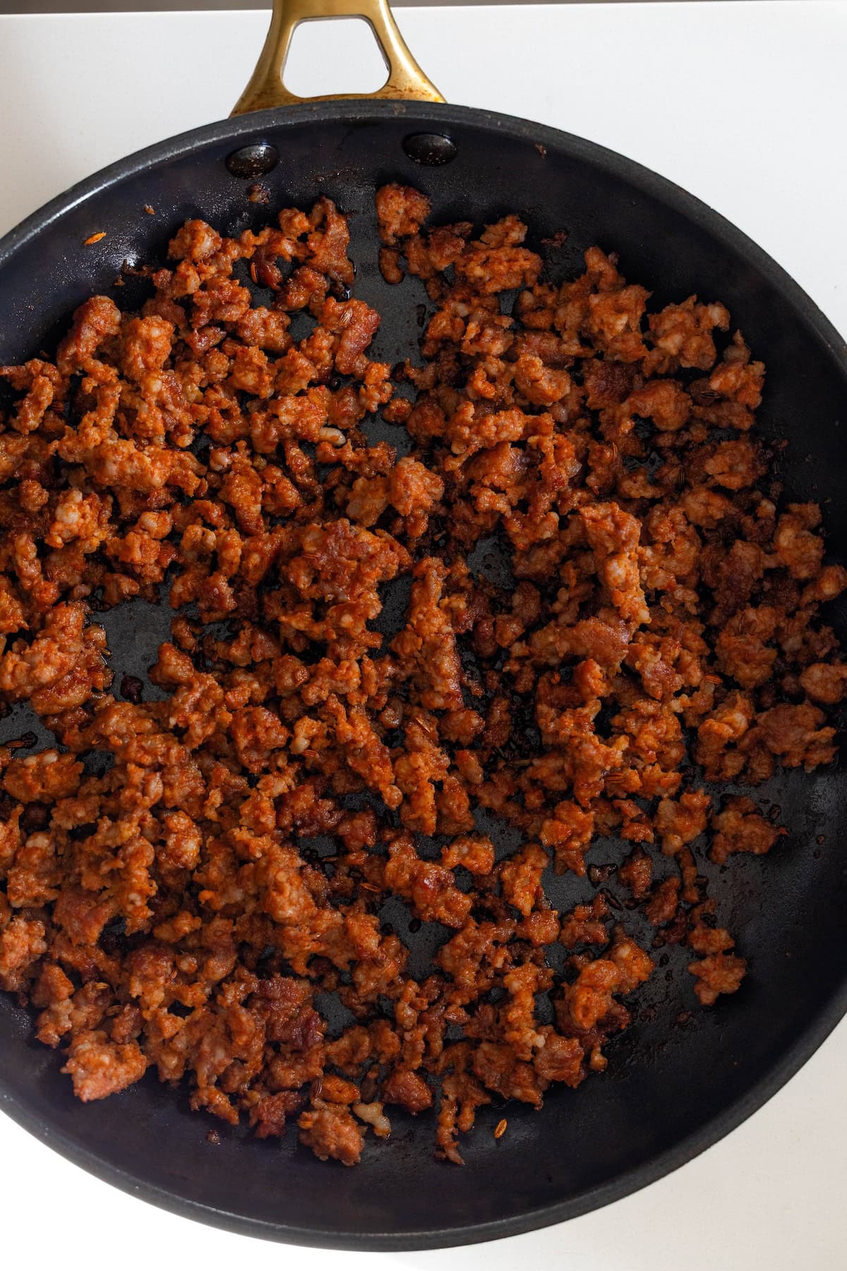 Cooked, crumbled seasoned ground meat in a black skillet with a brass handle, viewed from above—perfect for layering into a cheesy pasta dish or topping flavorful Cheesy Baked Rigatoni.