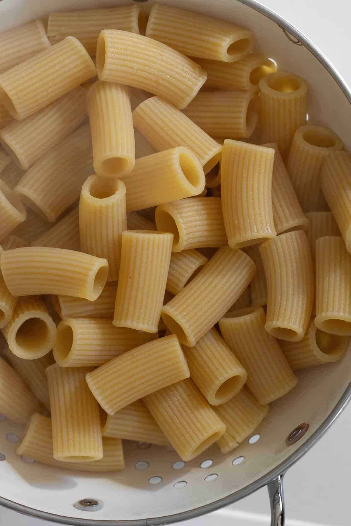 Cheesy baked rigatoni pasta draining in a white colander.