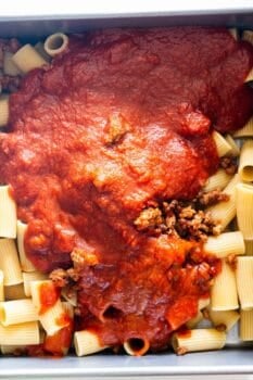 Cooked rigatoni pasta topped with ground meat and tomato sauce in a rectangular baking dish, perfect for making Cheesy Baked Rigatoni or your favorite baked pasta recipe.