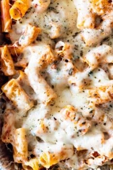 Close-up of cheesy baked rigatoni topped with melted cheese and sprinkled herbs.