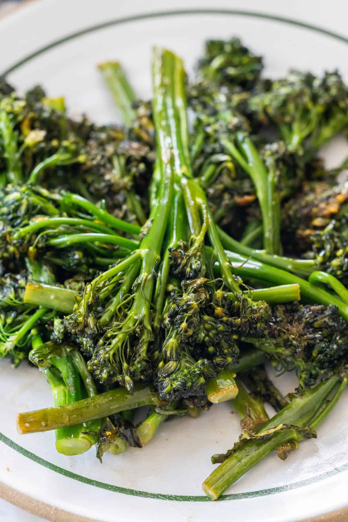 A plate of cooked broccolini with slightly charred edges, served on a white plate with a green rim.