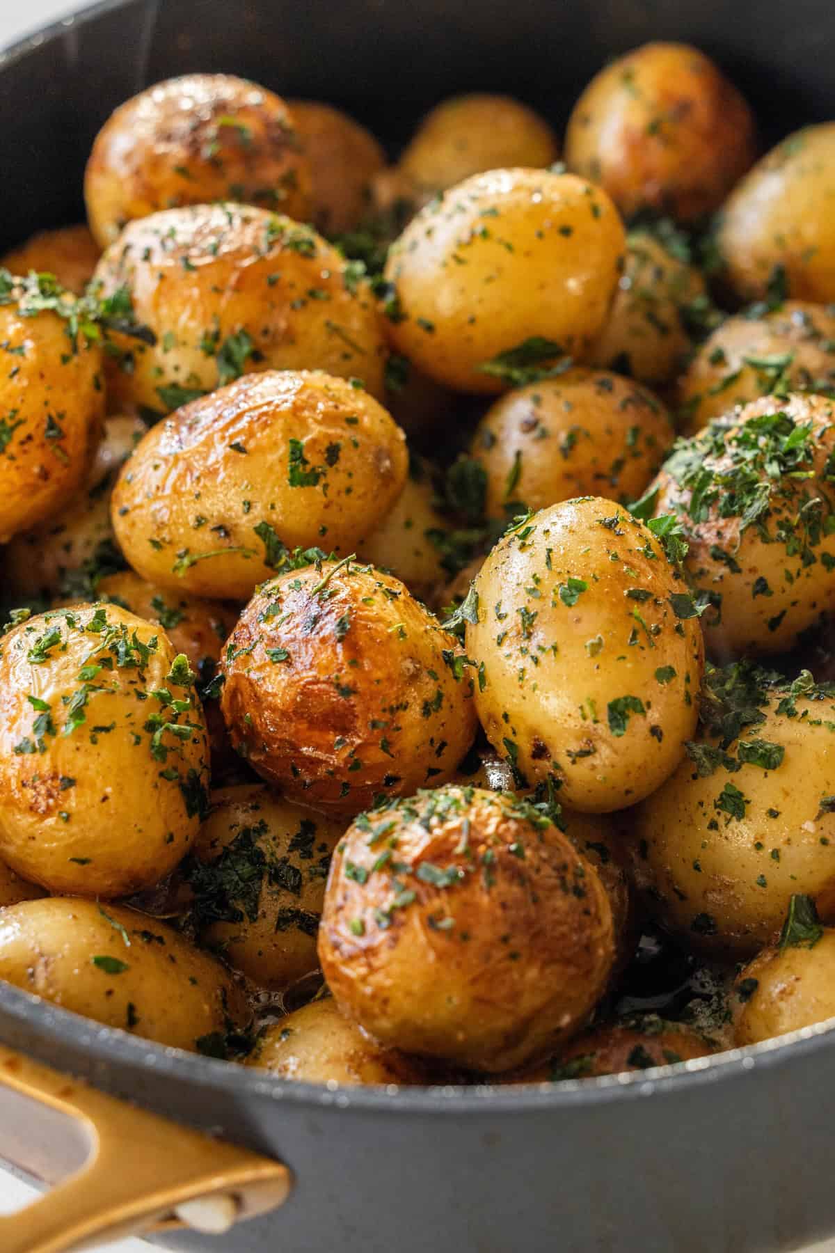 Close-up of Butter Poached Potatoes, perfectly seasoned with herbs, in a black pan.