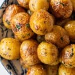 A bowl filled with roasted butter potatoes seasoned with herbs and spices.