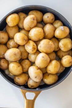 A pan filled with whole, unpeeled baby potatoes, some with light dirt spots, on a white surface—perfect for making butter poached potatoes.