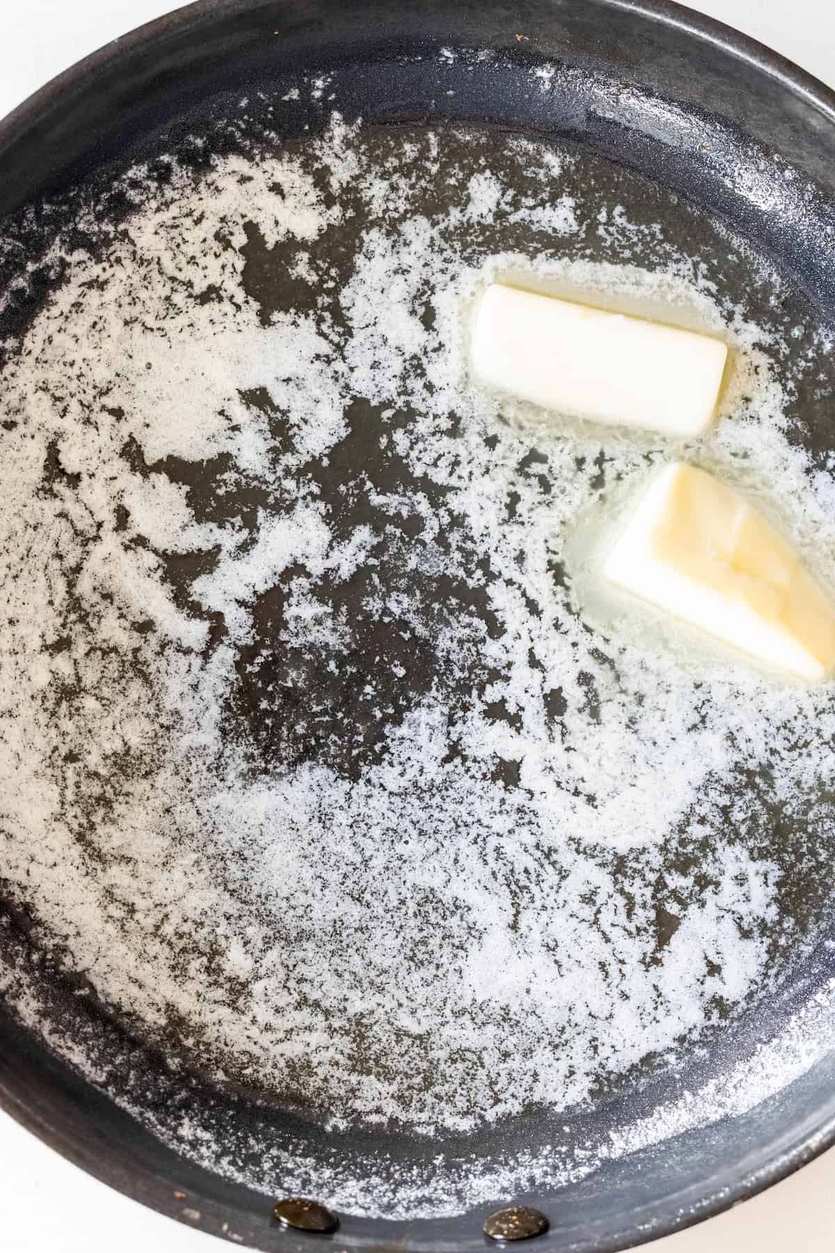 Two pieces of butter melting in a black skillet on a stove, perfect for starting delicious Butter Poached Potatoes.