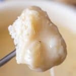 A piece of bread covered in melted cheese held on a fork above a bowl, capturing the irresistible allure of the best cheese fondue.