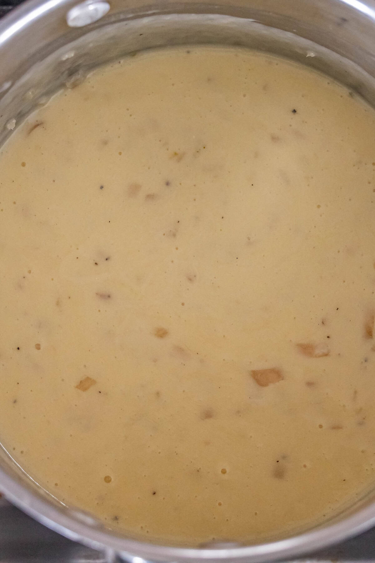 A saucepan filled with creamy, light yellow gravy—reminiscent of the best cheese fondue—nestled with small bits of onion or seasoning.