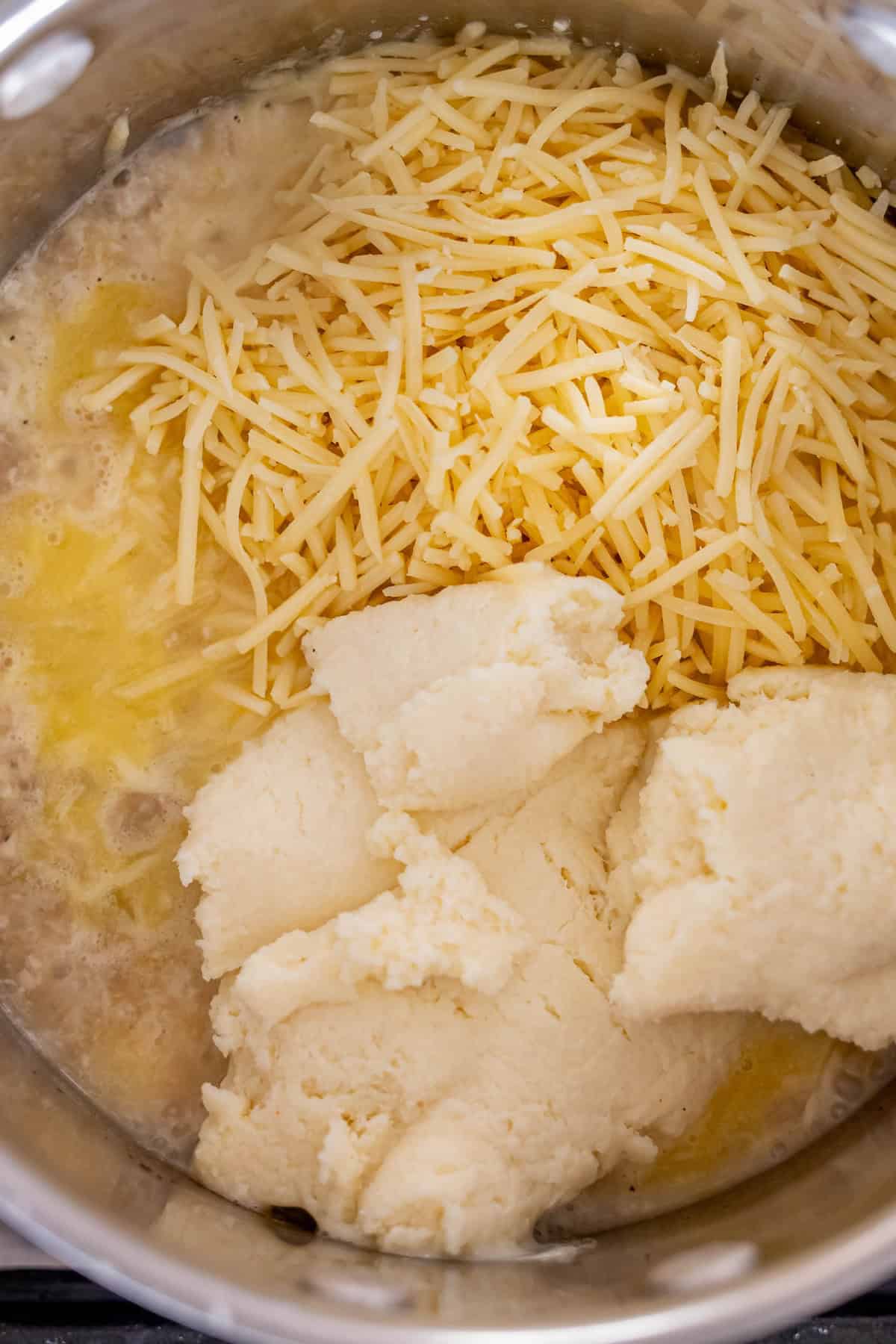 A pot containing shredded cheese and a cooked flour-butter mixture, likely in the process of making the best cheese fondue or a delicious cheese sauce.