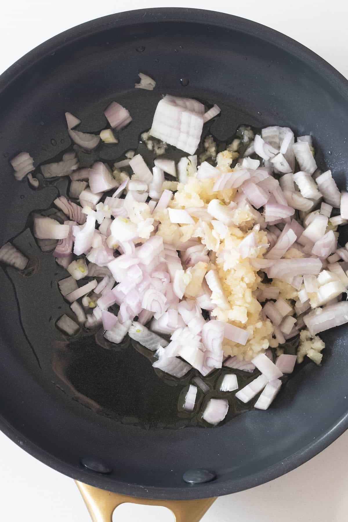 Chopped onions and minced garlic sizzle in a black skillet with oil, creating a flavorful base perfect for any fondue recipe or the best cheese fondue.