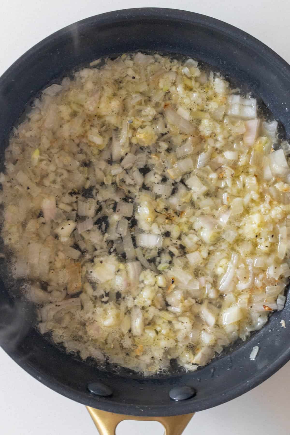 Diced onions and garlic sautéing in oil in a black frying pan—the perfect savory base for the best cheese fondue.