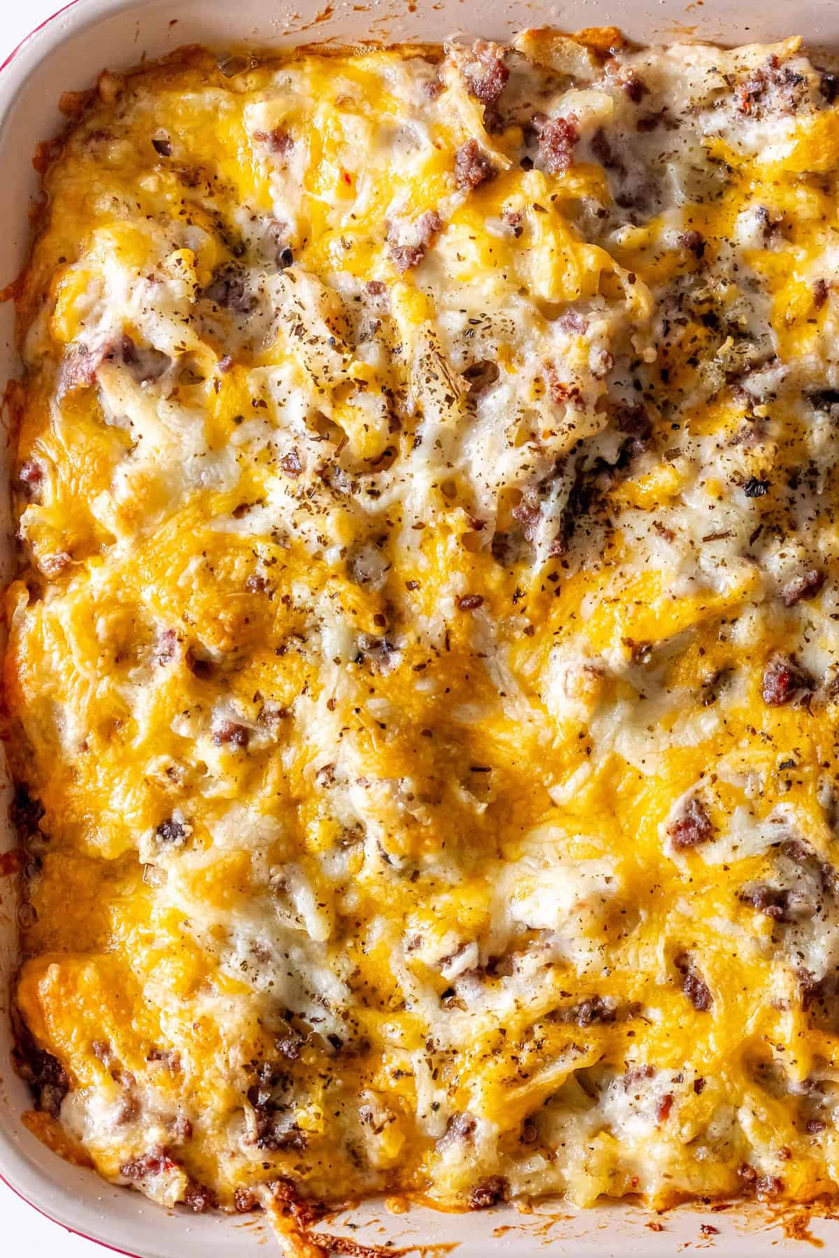 A baked cheesy ground beef casserole in a white dish, topped with melted cheddar cheese, hearty ground meat, and a sprinkling of herbs.