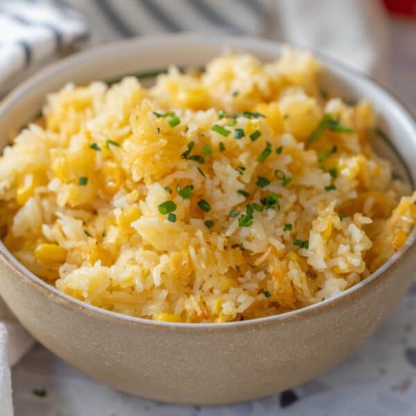 A bowl of cheesy corn rice casserole mixed with sweet corn and topped with fresh chopped chives.
