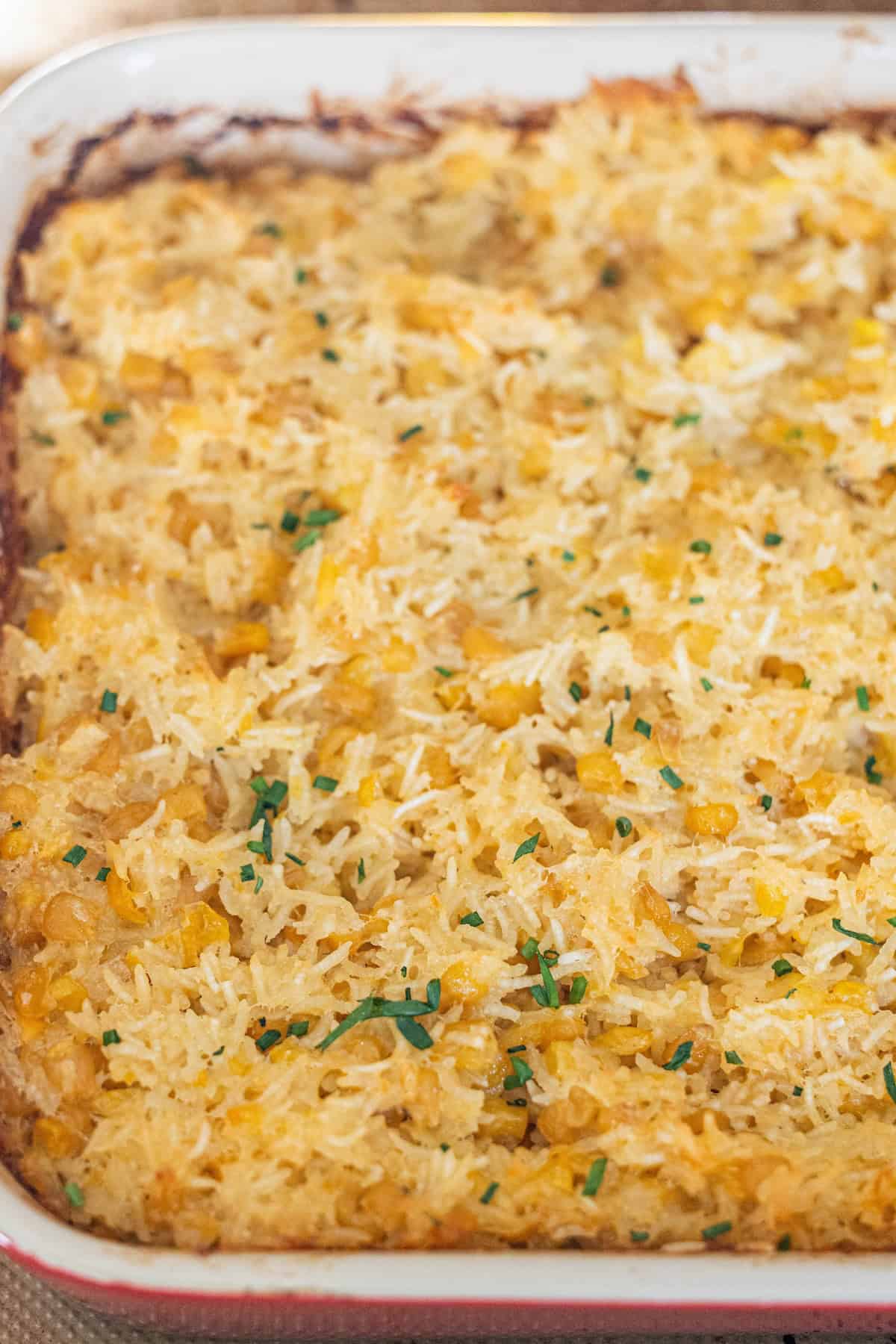 A Cheesy Corn Rice Casserole featuring a golden-brown rice and corn mixture, topped with chopped green herbs, makes for a comforting baked casserole dish.