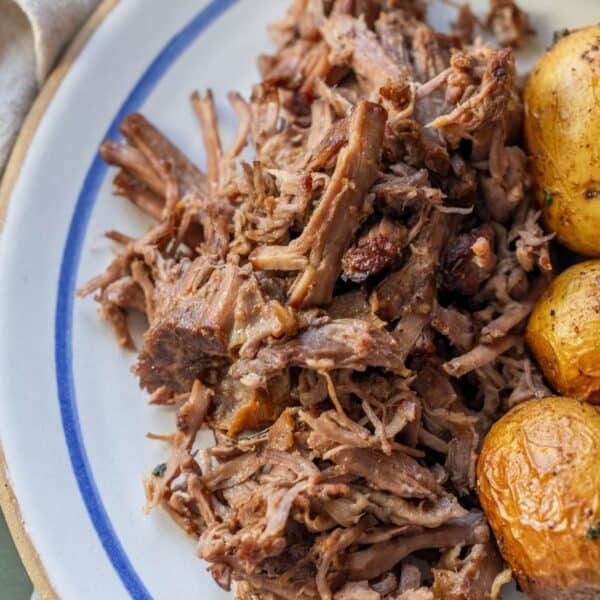 Tender Slow Cooker Chuck Roast, shredded and served on a plate alongside golden roasted baby potatoes.
