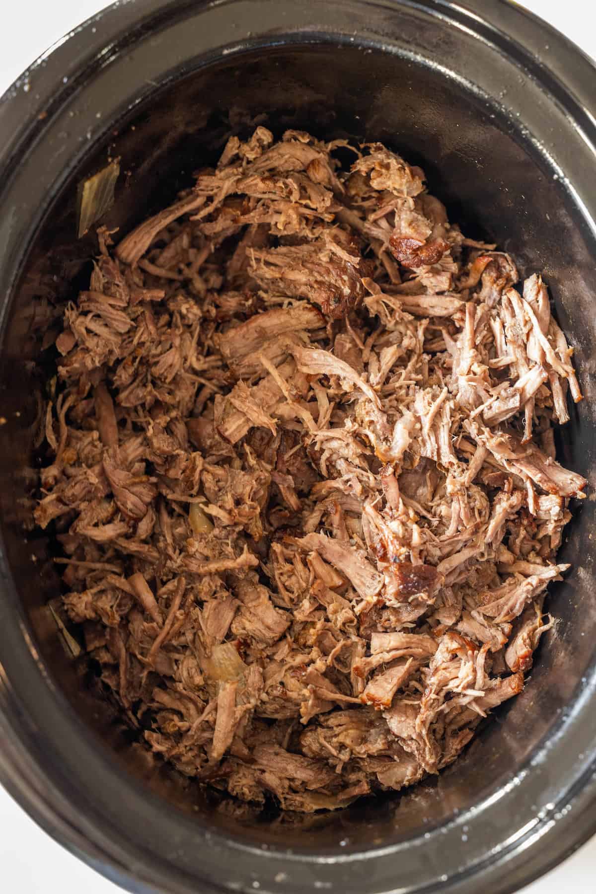Tender shredded beef, perfectly cooked as a Slow Cooker Chuck Roast, inside a black slow cooker and ready to serve.