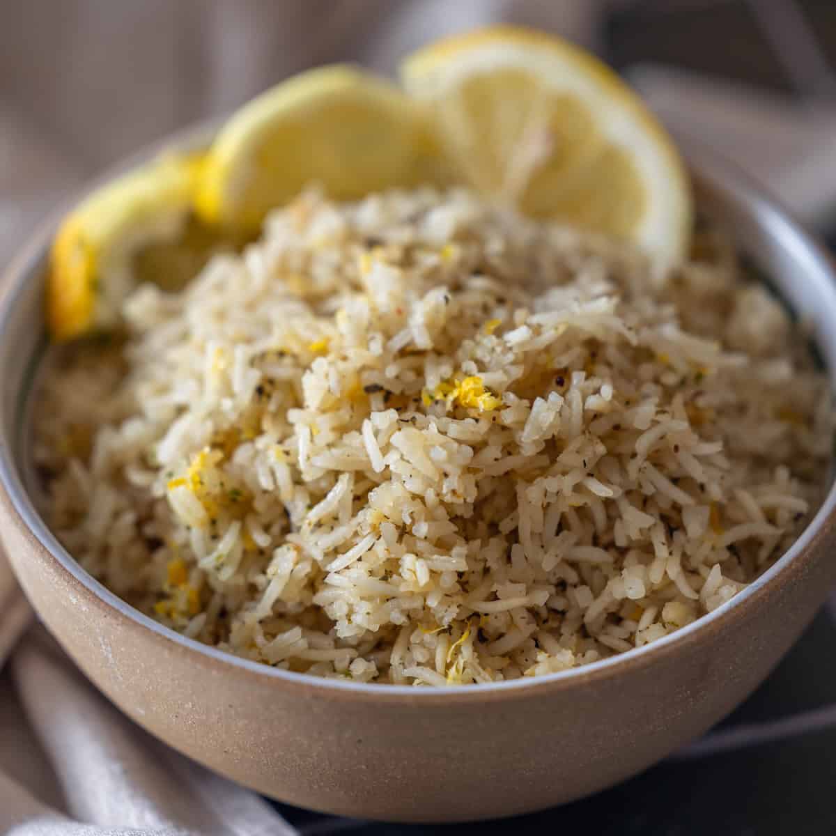 A bowl of Baked Lemon Rice garnished with lemon zest, served with three lemon slices on the rim.