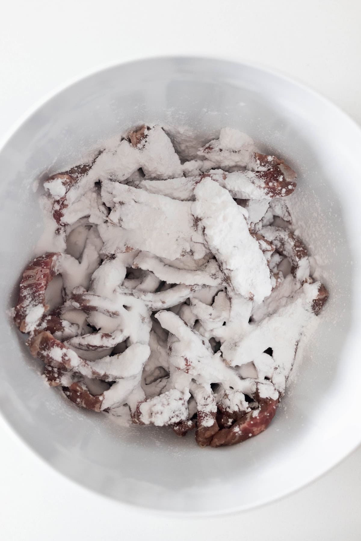Easy Mongolian Beef: sliced meat pieces coated with white flour or starch in a white bowl, perfect for recreating takeout style at home.