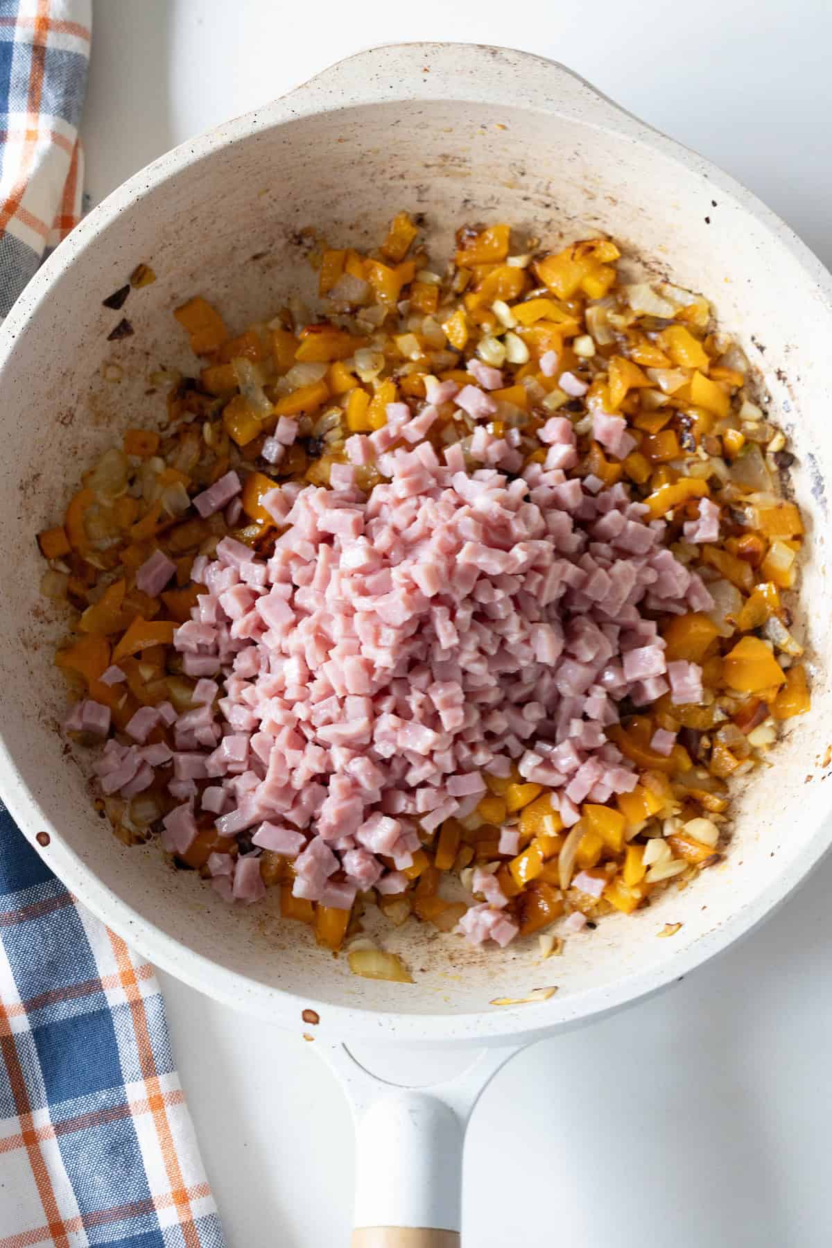 Chopped ham sits atop saut&eacute;ed yellow bell peppers and onions in a white skillet, adding a savory touch reminiscent of an Old Fashioned Ham and Beans dish.