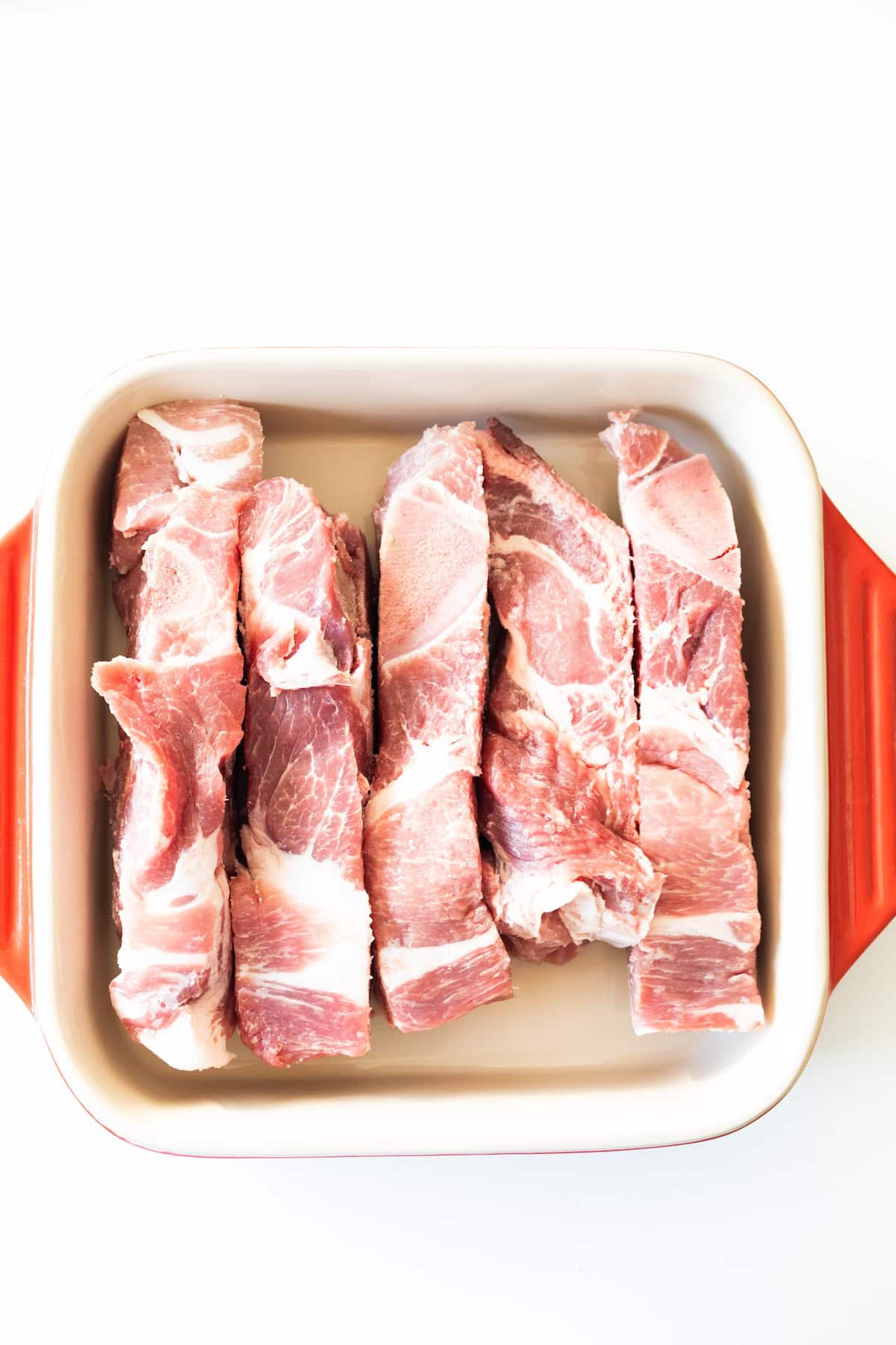 Country Style Ribs are arranged in a single layer inside a rectangular baking dish with orange handles, on a white background.