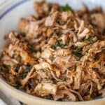 A close-up of a bowl filled with shredded, cooked country style ribs garnished with chopped herbs.