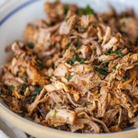 A close-up of a bowl filled with shredded, cooked country style ribs garnished with chopped herbs.