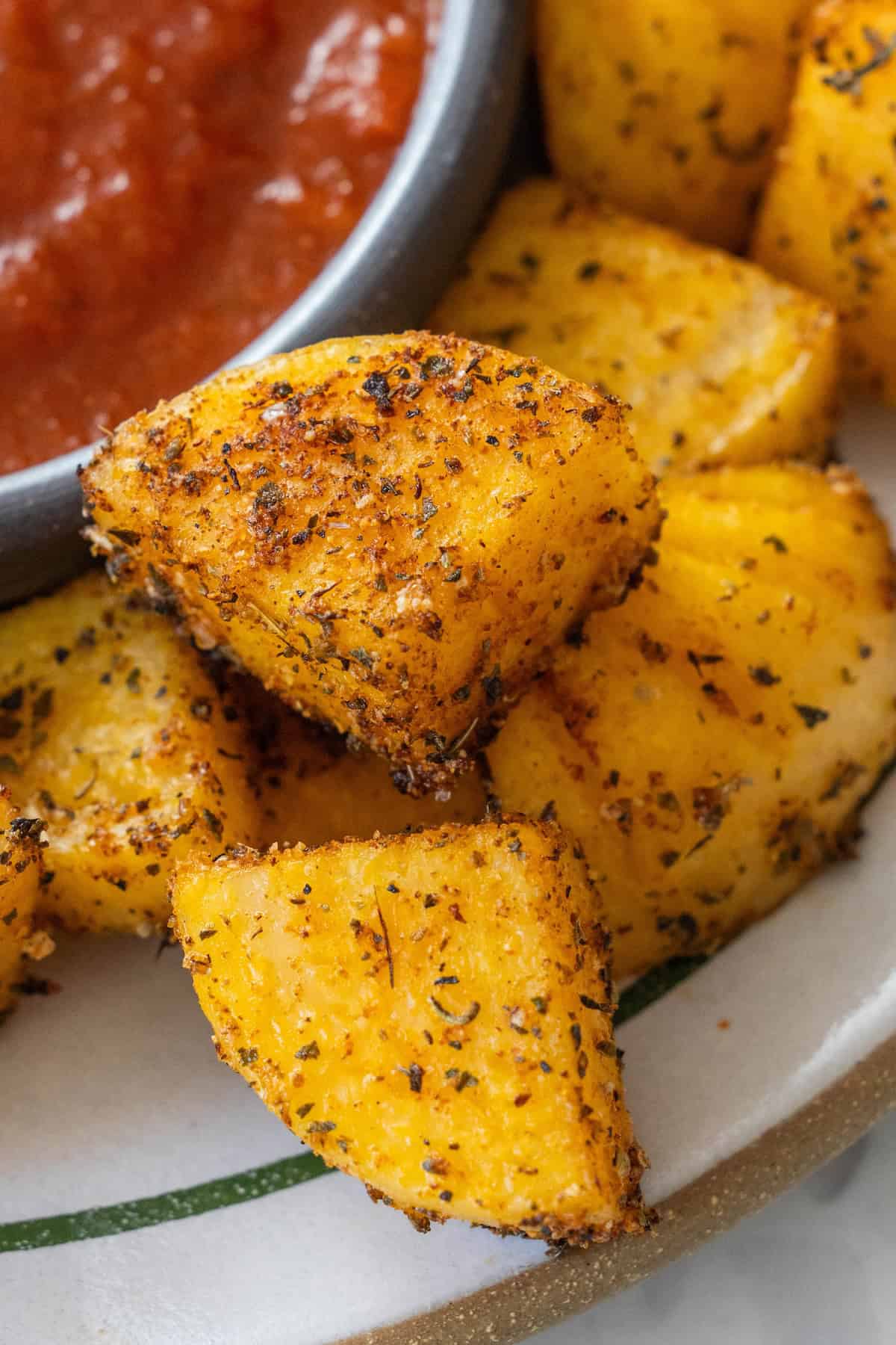 Seasoned roasted potato wedges are arranged on a plate next to a bowl of red dipping sauce, creating an inviting assortment of baked appetizers.