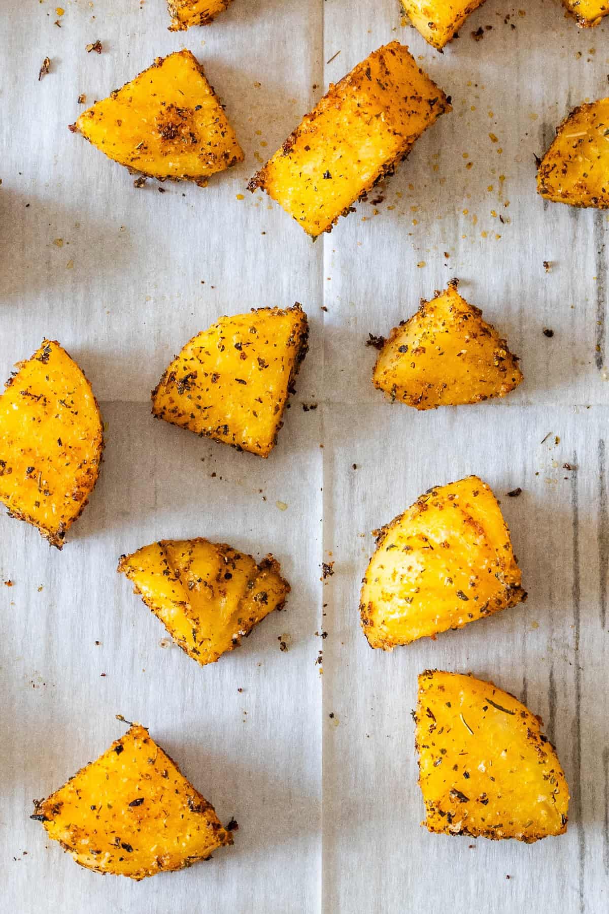 Roasted golden beet wedges coated with herbs and spices make a vibrant baked appetizer, beautifully arranged on a sheet of parchment paper.