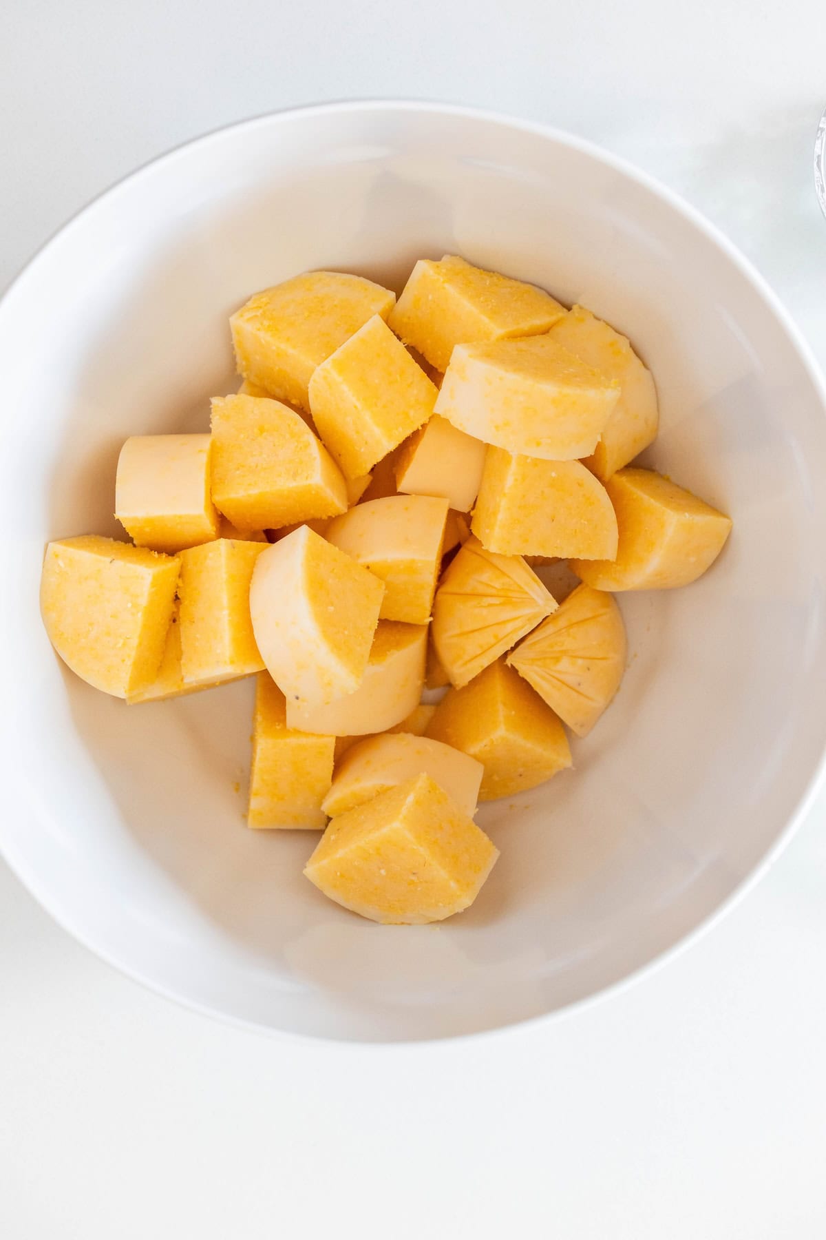 A white bowl containing several chunks of peeled and cut yellow yam, perfect alongside Baked Polenta Bites, sits on a white surface.