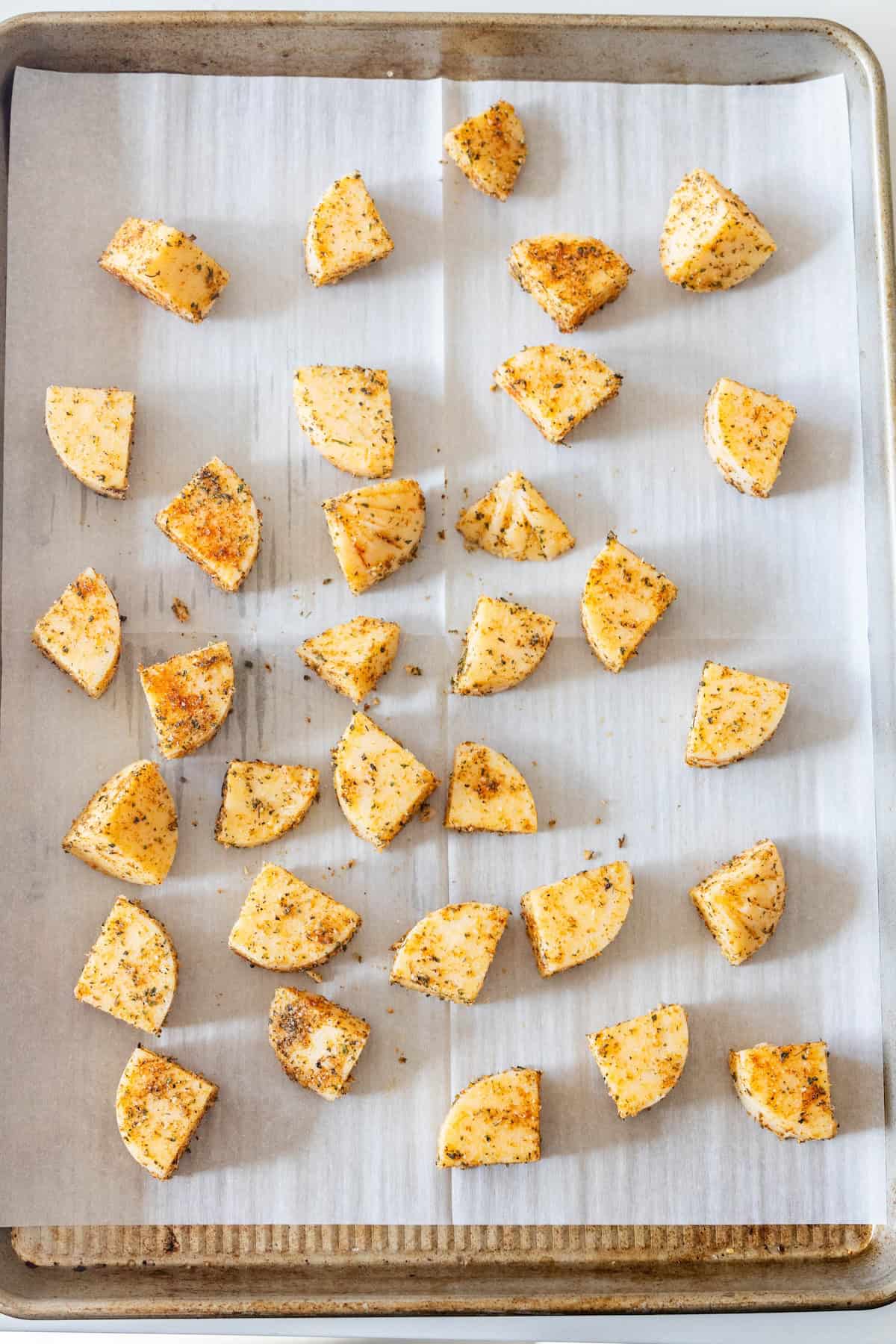 Seasoned potato wedges are arranged on a parchment-lined baking sheet, ready for roasting alongside delicious Baked Polenta Bites.