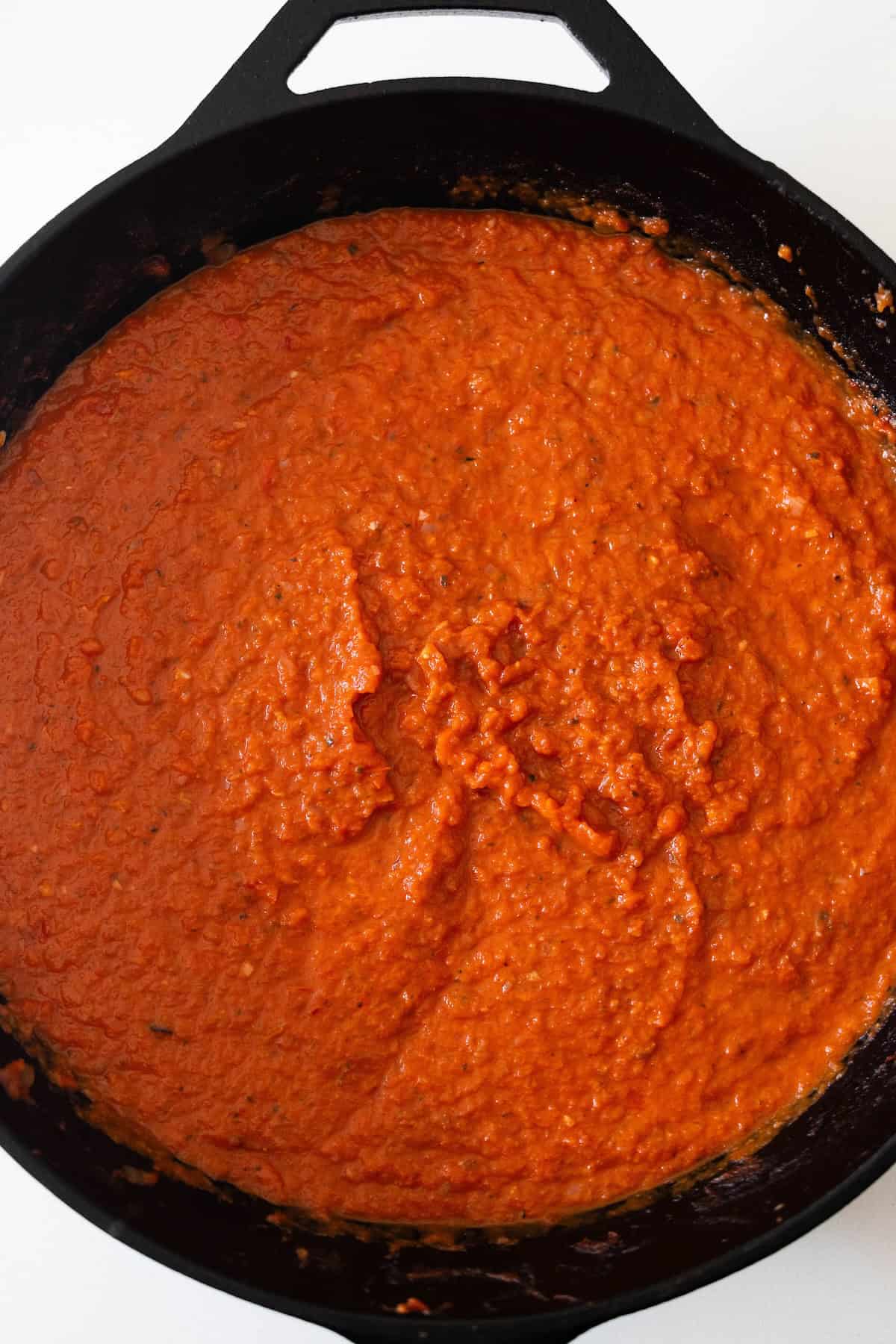 A cast iron skillet filled with a thick, red-orange tomato-based sauce, spread evenly across the surface—the perfect start for an easy shakshuka recipe.