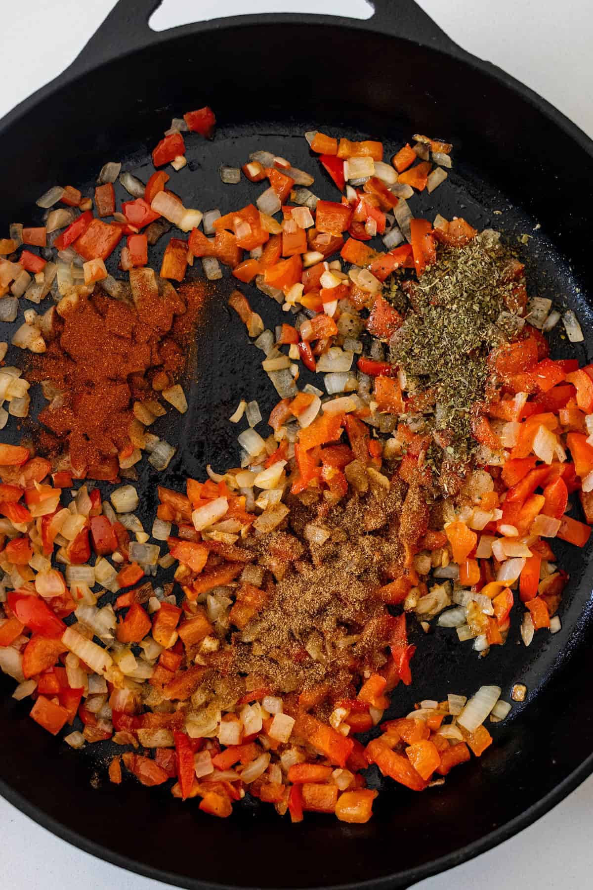 Chopped onions and red bell peppers sautéing in a cast iron skillet with paprika, dried herbs, and ground cumin—the perfect base for an Egg Breakfast or classic Shakshuka Recipe.