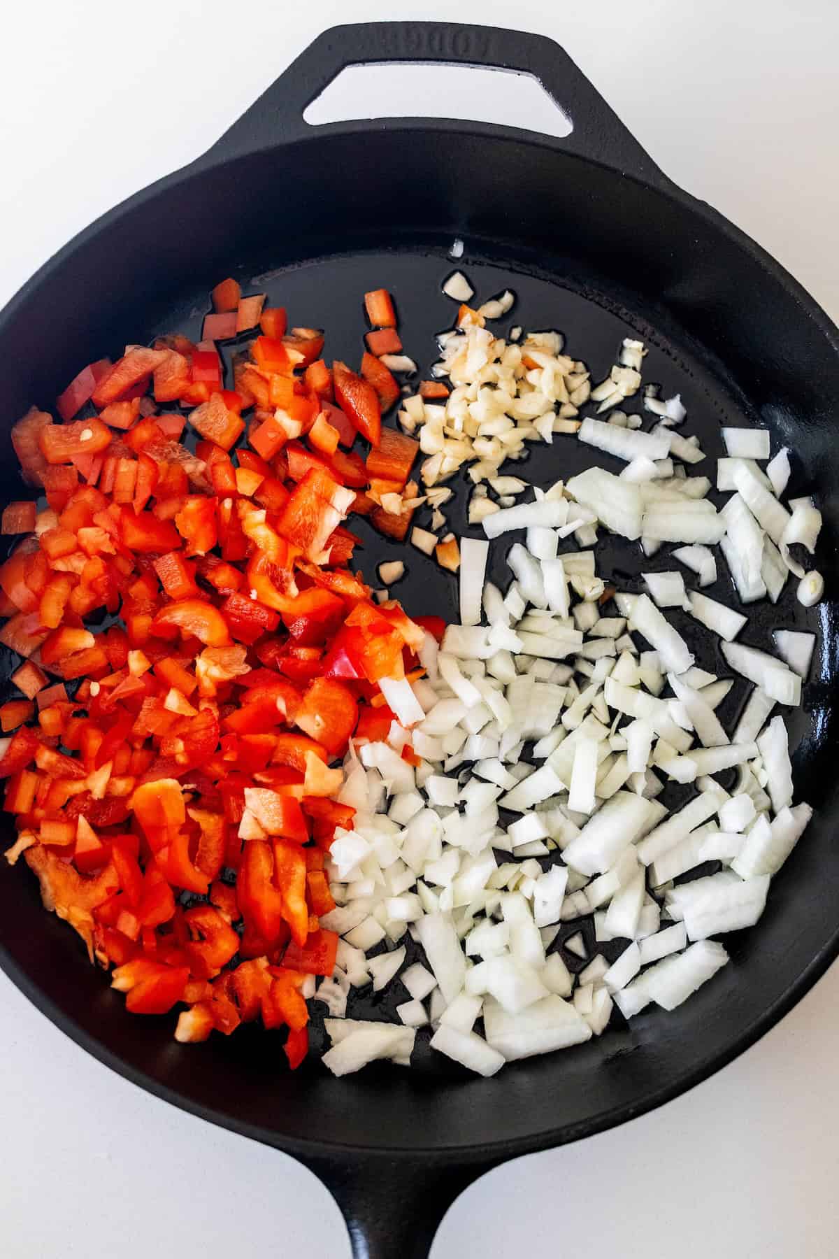 A cast iron skillet with chopped red bell pepper, white onion, and minced garlic arranged separately—perfect prep for starting a classic Shakshuka recipe.