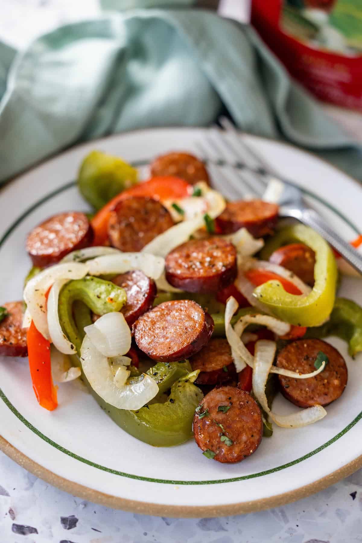A plate of sliced kielbasa, sautéed onions, and peppers, with a fork placed beside the food.