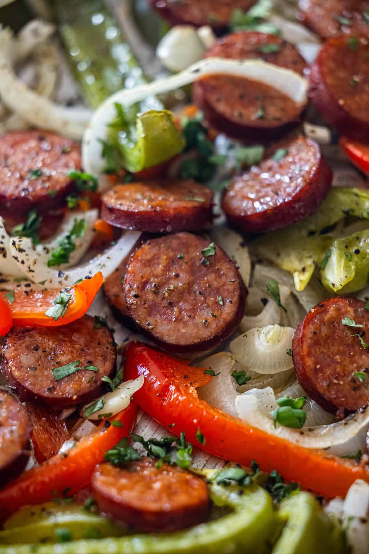 Sliced sausage, onions, and colorful peppers seasoned with herbs, arranged for a flavorful Sheetpan Kielbasa dinner.