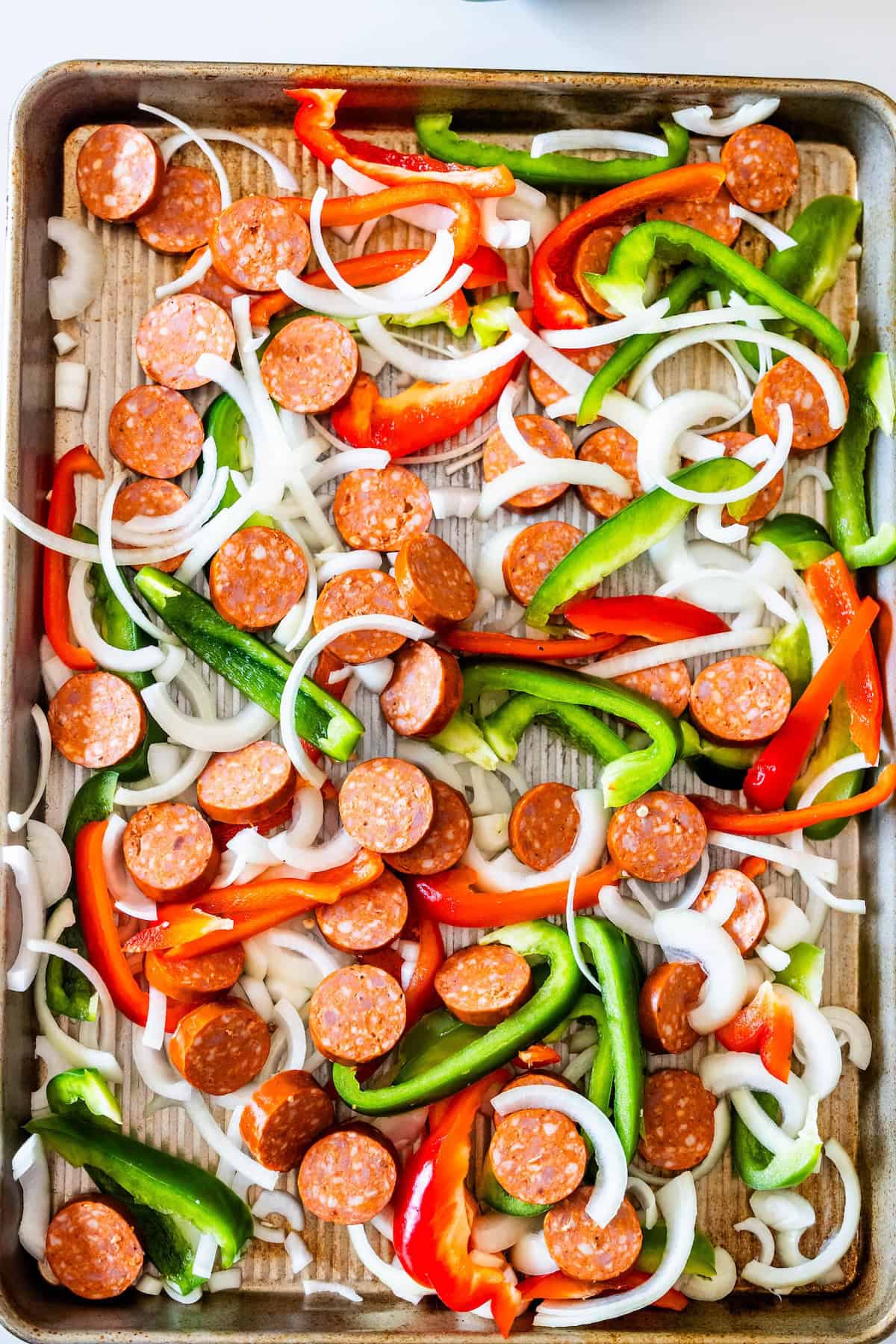 A baking sheet topped with sliced pepperoni, green and red bell peppers, onion slices, and hearty kielbasa makes for an easy Sheetpan Dinner—all spread out and ready for cooking.