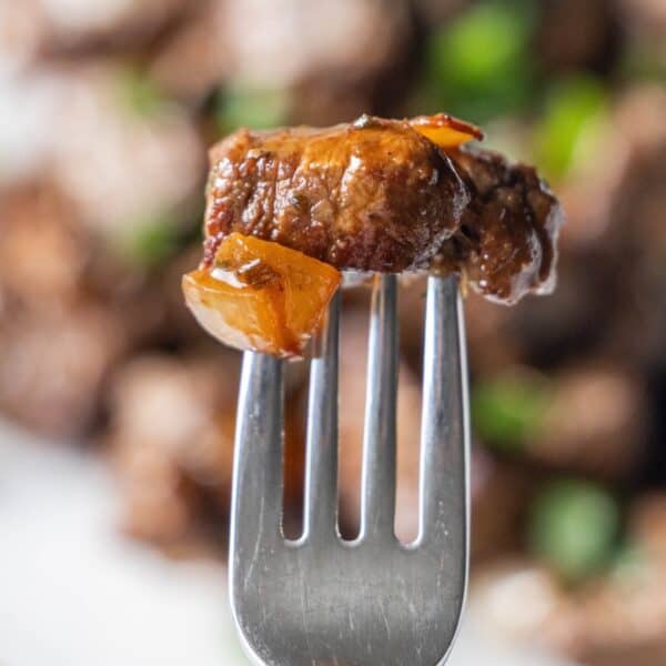 A close-up of a fork holding a juicy piece of cooked sirloin steak with a small piece of onion. The background is blurred.