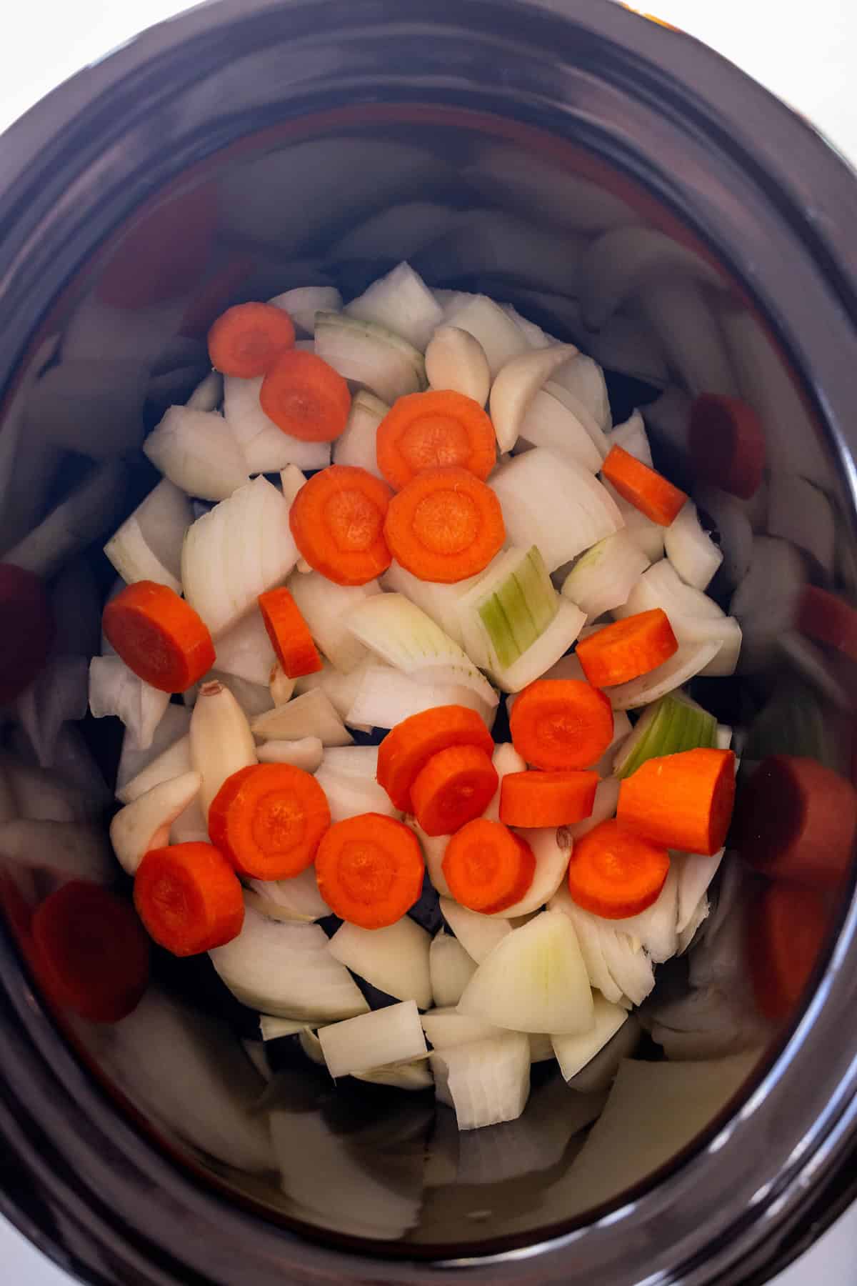 Chopped onions, carrots, celery, and garlic are placed at the bottom of a slow cooker—perfect for creating a flavorful Slow Cooker Chuck Roast.