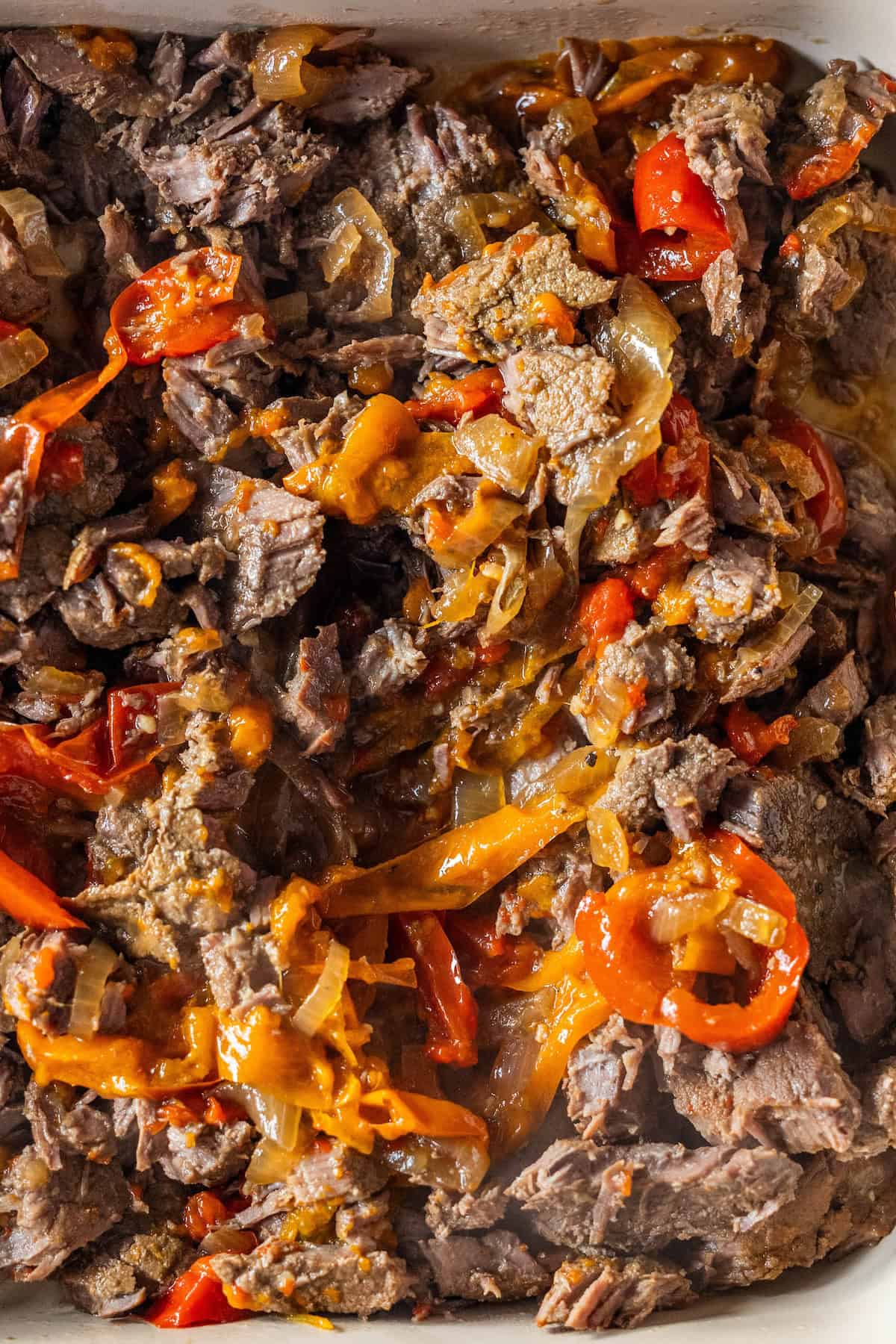 Cooked beef strips mixed with saut&eacute;ed onions and red bell peppers, seasoned to perfection&mdash;just like classic Philly Cheesesteaks&mdash;in a savory close-up view.