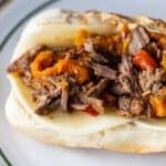 A classic Philly Cheesesteak on a hoagie roll filled with sliced beef, melted cheese, and chopped cooked peppers, served on a white plate.