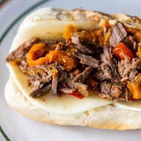 A classic Philly Cheesesteak on a hoagie roll filled with sliced beef, melted cheese, and chopped cooked peppers, served on a white plate.