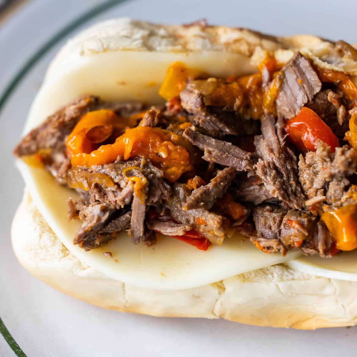 A classic Philly Cheesesteak on a hoagie roll filled with sliced beef, melted cheese, and chopped cooked peppers, served on a white plate.