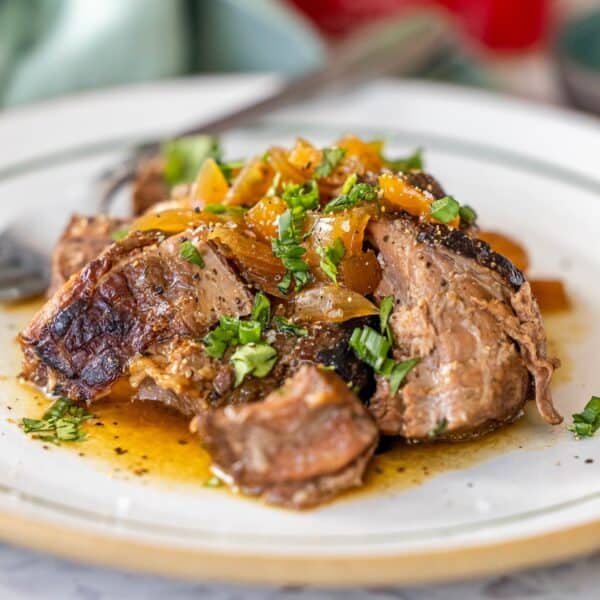 A plate of Slow Cooker Sirloin Steak topped with sautรฉed onions and chopped herbs, served in a light sauce.