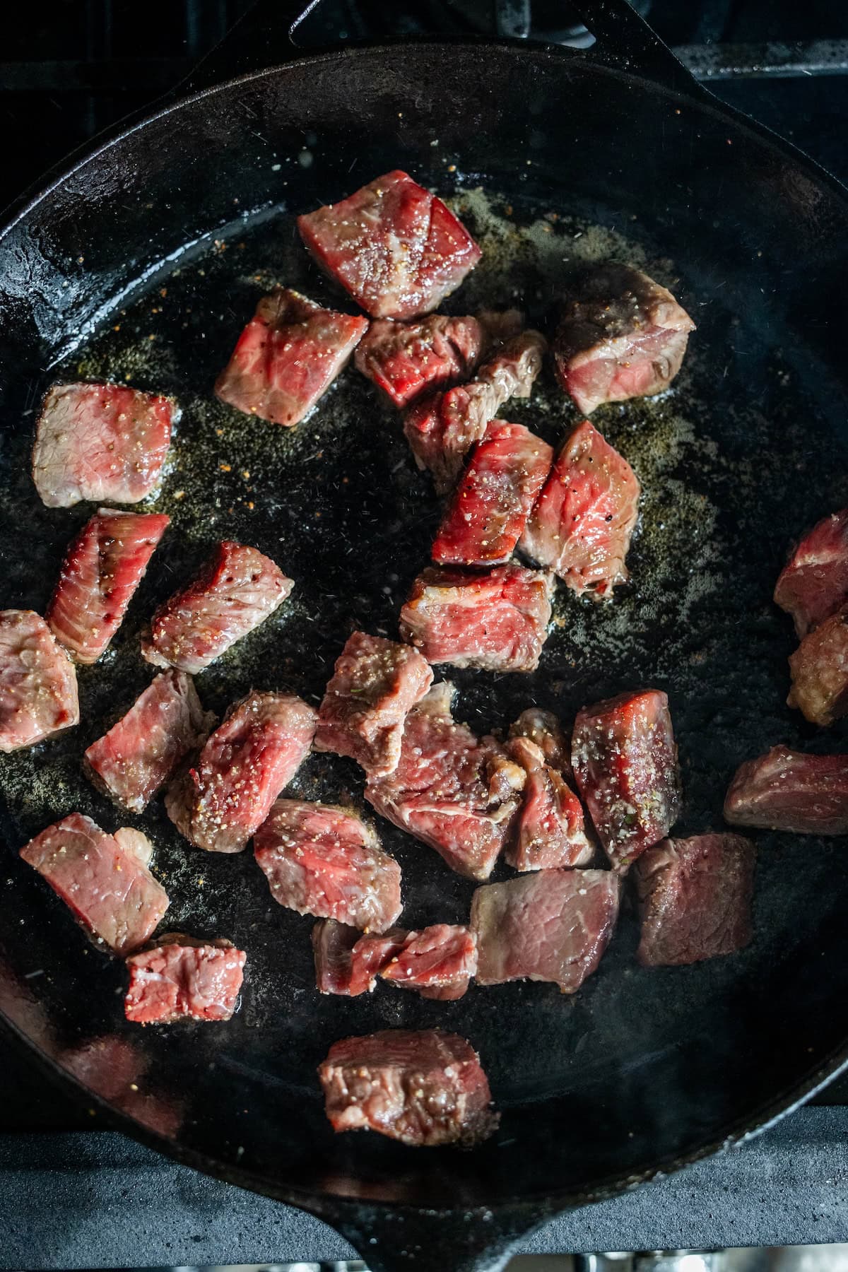 Sirloin Steak Tips are searing in a black cast iron skillet, their browned exterior sizzling in oil for flavorful pan seared steak tips.